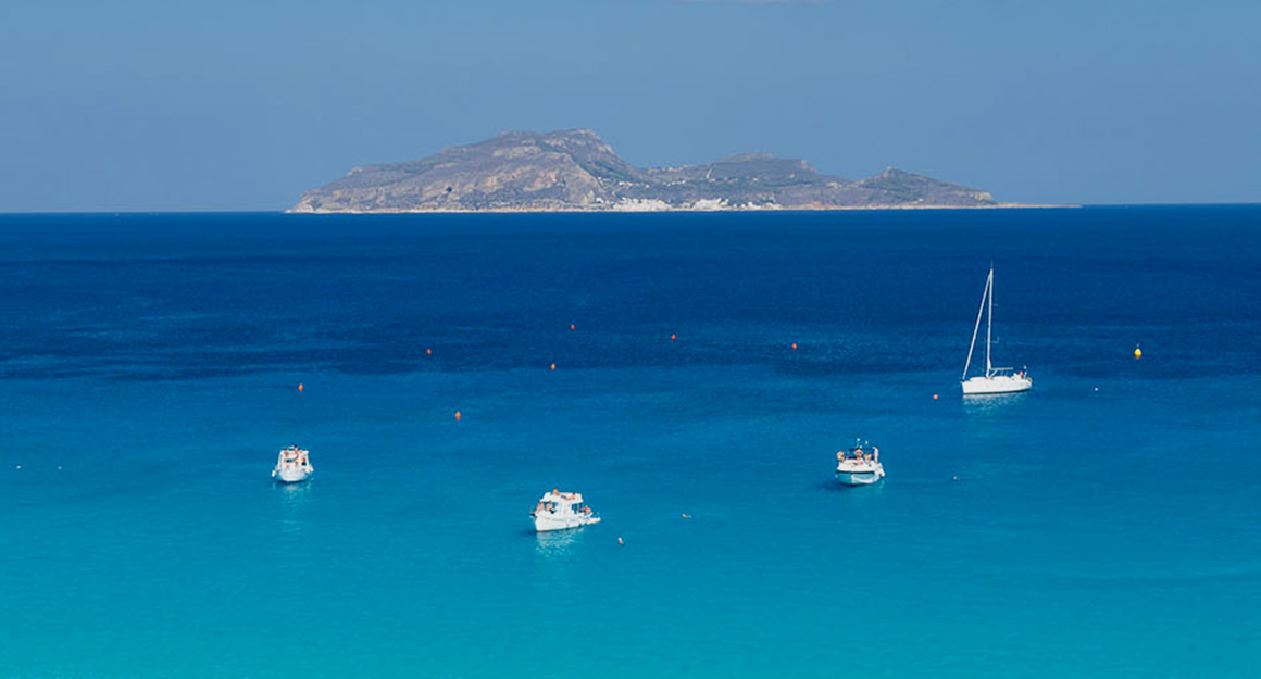 A huge, clear, deep blue bay with four boats and a large island on the horizon.