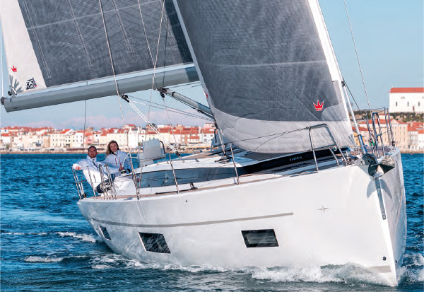 Sailing yacht from the front on the water with coastal town in the background.